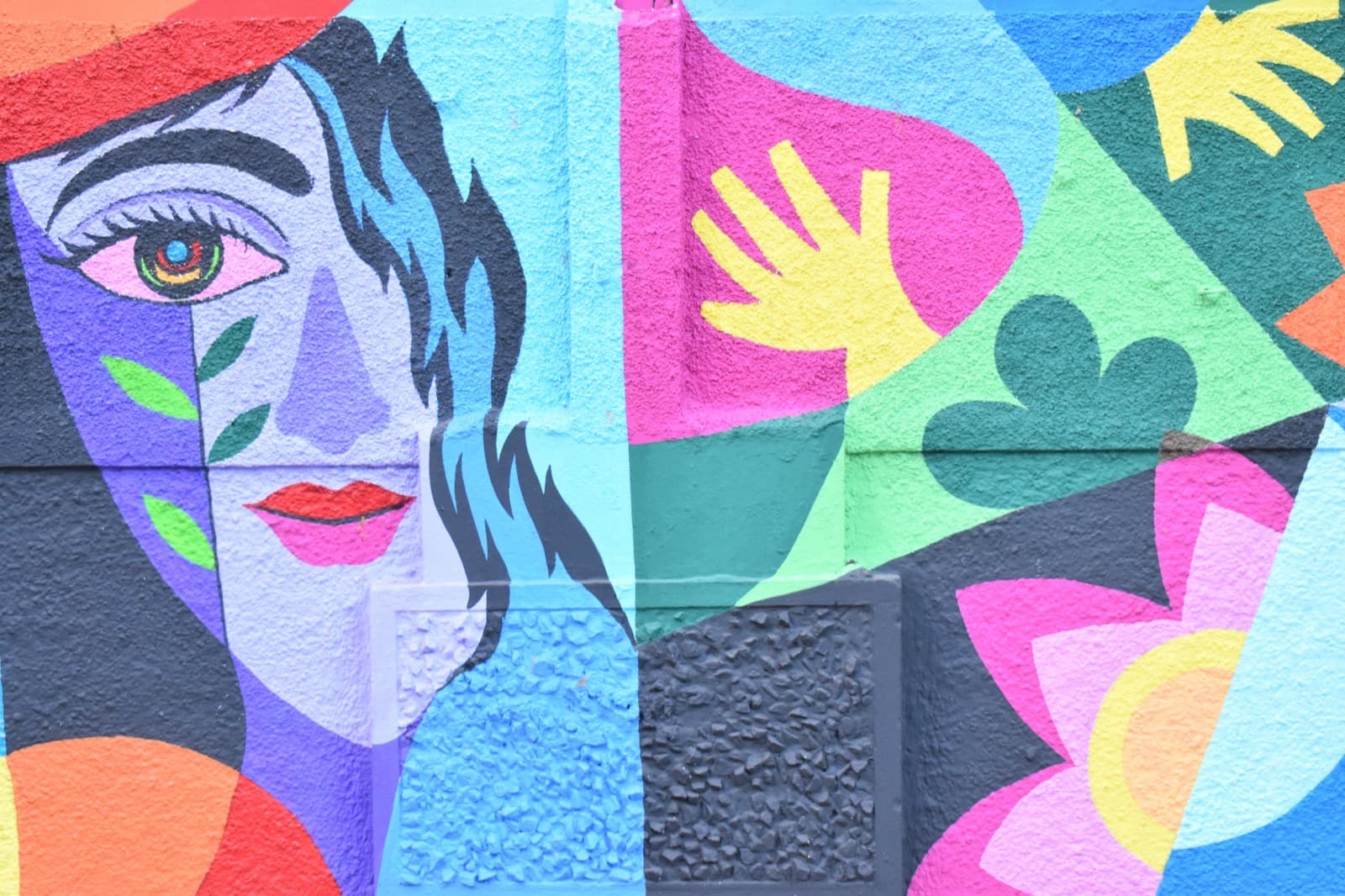 Colorful cubist-style mural of a woman's face with a hand and leaf motifs