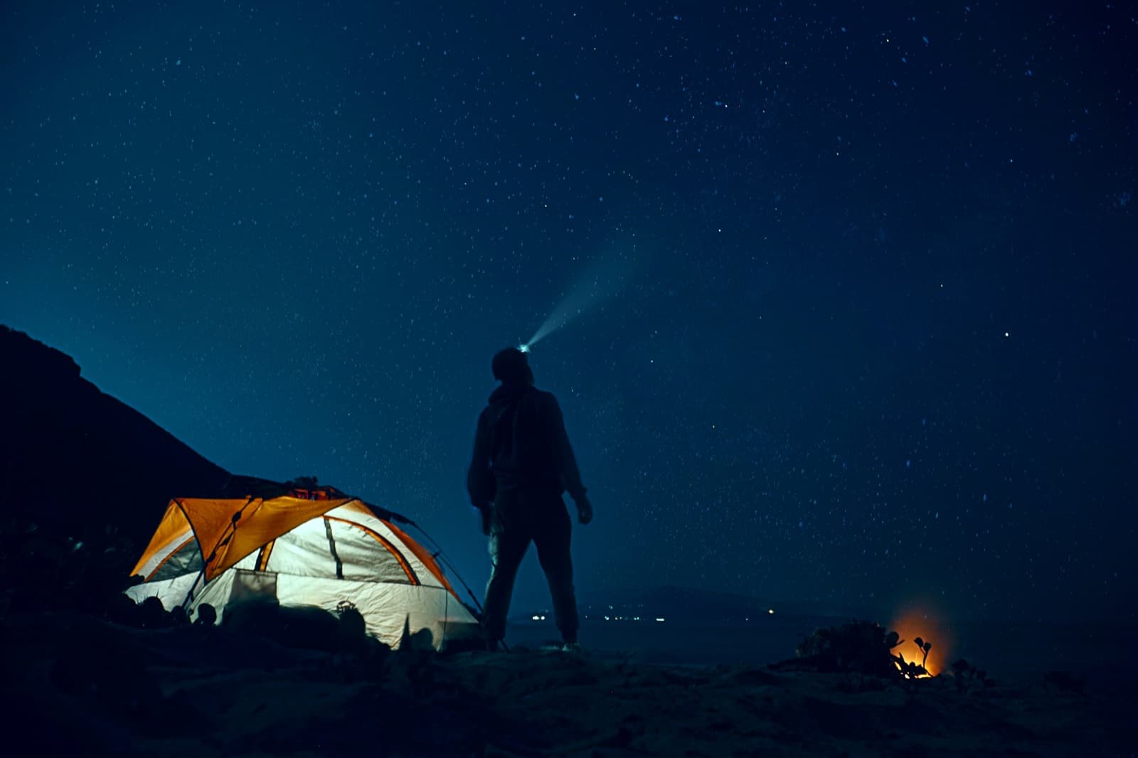 A man sitting alone under the stars next to a tent and campfire