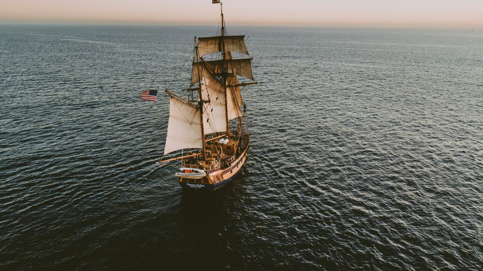 A sailing ship moving across open water at golden hour