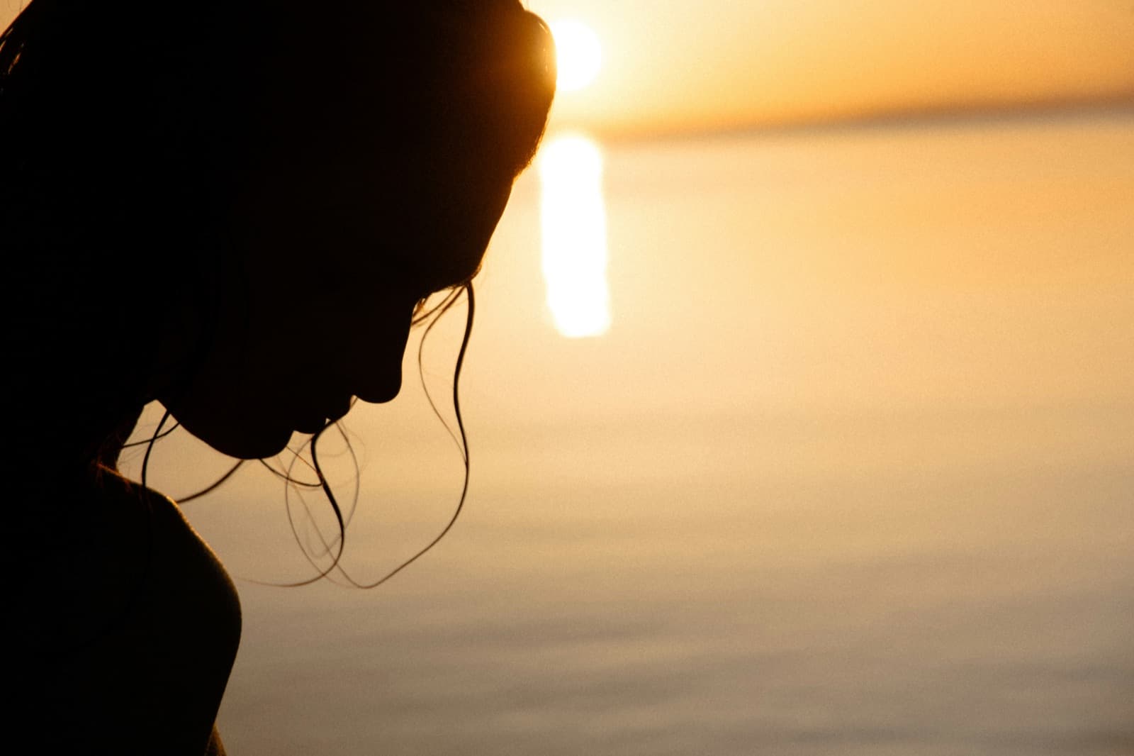 Silhouette of a woman looking down with golden sunrise light over the sea behind her